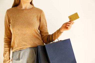 Klasik şık kıyafet, kahverengi süveter ve gevşek gri pantolon alışverişe gitti genç ince kadın, holding kağıt torba ve VIP altın kredi / bankamatik kartı. Beyaz arka plan, kopya alanı, yakın çekim.