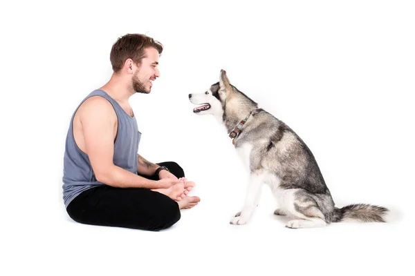 Young bearded man hanging out out with his husky dog. Hipster male wearing plain blank grey tank top spending quality time with four legged pet friend. Close up, copy space, background