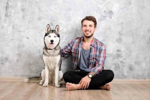 Young bearded man hanging out out with his husky dog. Hipster male wearing checkered flannel shirt and grey tank top spending quality time with four legged pet friend. Close up, copy space, background