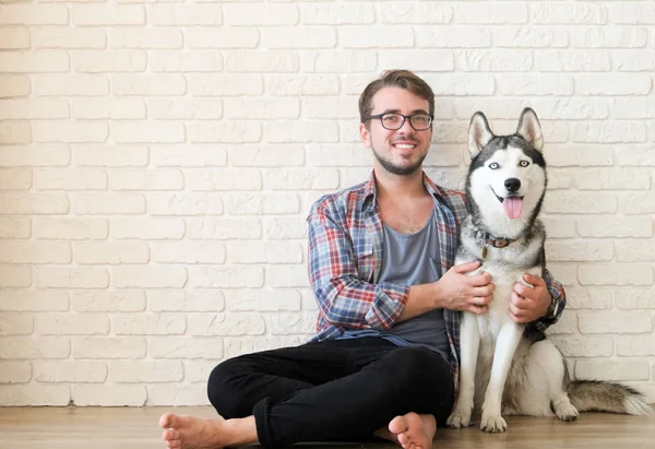 Genç sakallı adam dışarı asılı dışarı ile onun husky köpek. Hippi erkek damalı pazen gömlek ve gri dört bacaklı evde beslenen hayvan arkadaş ile kaliteli zaman geçirmek tişört giyiyor. Yakın çekim, uzay, arka plan kopya