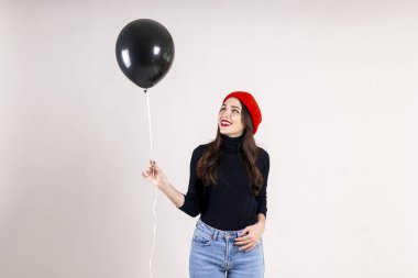 Siyah boğazlı kazak, kot anne ve kırmızı bere, boş helyum balonu tutan giyen güzel hipster genç kadın parlak kırmızı ruj makyaj ile. Tatil kutlama kavramı. Arka plan, kopya alanı.
