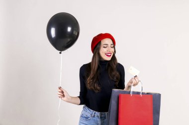 Balıkçı yaka, Anne kot, kırmızı bere, holding boş balon ve renkli alışveriş torbaları giyen güzel hipster genç kadın parlak kırmızı ruj. Siyah Cuma satış konsepti. Arka plan, kopya alanı.