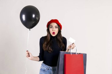 Balıkçı yaka, Anne kot, kırmızı bere, holding boş balon ve renkli alışveriş torbaları giyen güzel hipster genç kadın parlak kırmızı ruj. Siyah Cuma satış konsepti. Arka plan, kopya alanı.