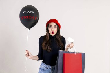 Güzel hipster genç kadın giyiyor balıkçı yaka, Anne kot, kırmızı bere, holding balon w / metin ve renkli alışveriş torbaları parlak kırmızı ruj. Siyah Cuma satış konsepti. Arka plan, kopya alanı.