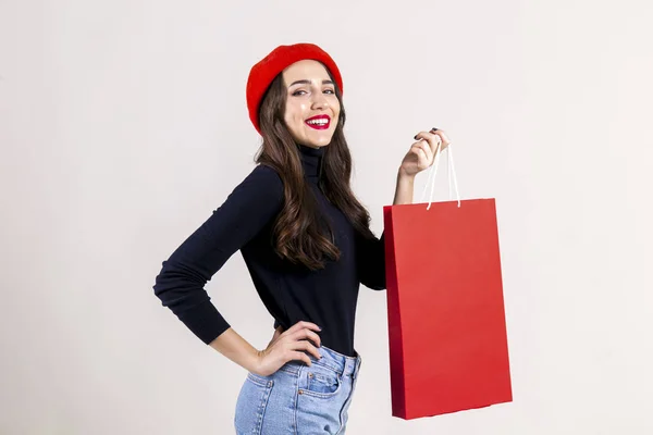 美丽的时髦的年轻妇女与明亮的红色口红妆 穿着黑色高领 妈妈牛仔裤和红色贝雷帽 拿着空白购物袋 秋季假期销售季节概念 复制空间 — 图库照片