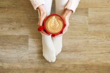 Cappuccino kahve içme ve ahşap katta oturan genç kadın. Üstten görünüm sıcak beyaz kadın bacak knee yüksek çorap. Konfor kış tatil kavramı. Yakın çekim, uzay, arka plan kopya.