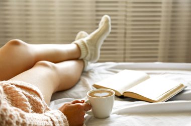 Tembel öğleden sonra kavram. Cappuccino kahve latte sanat köpük şeklinde kalp ile sahip eski kitap, okuma pencere sabah ışığında yatakta oturan kadın görüntüsünü kapatın. Arka plan, kopya alanı