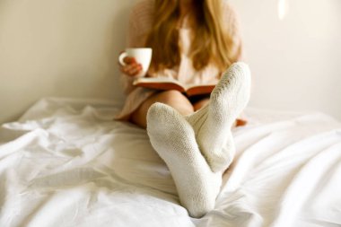 Tembel öğleden sonra kavram. Cappuccino kahve sahip eski kitap, okuma pencere sabah ışıkta beyaz duvara yaslanmış yatakta oturan kadın görüntüsünü kapatın. Arka plan, kopya alanı