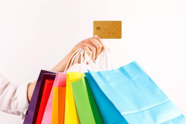 Farklı renkli boş alışveriş torbaları altın sınırsız kredi kartı ile demet izole beyaz arka plan üzerinde tutan el atış kırpılmış. Siyah Cuma satış konsepti. Uzay kopyalayın, yakın çekim.
