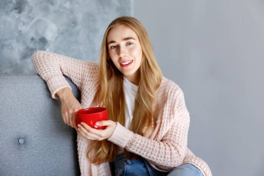 Gri tekstil koltukta evde beyaz t-shirt giyen genç güzel kadın. İç durum, kanepede onun yüce evinde istirahat çekici ince kadın. Arka plan, kopya alanı, yakın çekim.