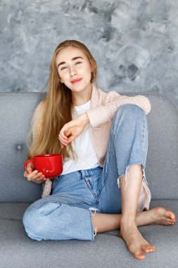 Gri tekstil koltukta evde beyaz t-shirt giyen genç güzel kadın. İç durum, kanepede onun yüce evinde istirahat çekici ince kadın. Arka plan, kopya alanı, yakın çekim.