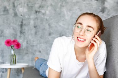 Gri tekstil koltukta evde beyaz t-shirt giyen genç güzel kadın. İç durum, kanepede onun yüce evinde istirahat çekici ince kadın. Arka plan, kopya alanı, yakın çekim.