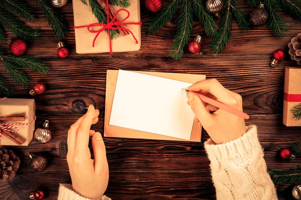 Noel hediyeleri ve dekorasyon üstten görünüm ile ahşap arka plan üzerinde Noel Baba'ya mektup yazma eller. Vintage görüntü kadınla tonda, Noel, düz için istek listesi yatıyordu, kopya alanı, arka plan.