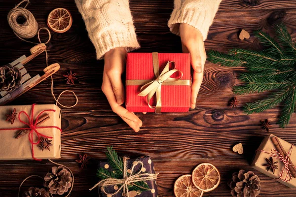 Top view of woman in white sweater getting ready for winter holiday season, wrapping presents and preparing decorations on wooden table. Background, copy space, flat lay,