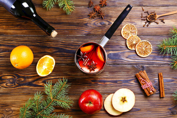 Christmas composition with mulled wine with its ingredients & spices on wooden textured table. Traditional drink on winter holiday season. Copy space, close up, top view, background.