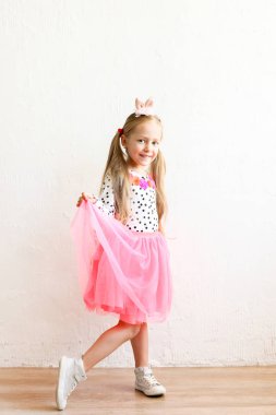 Paskalya bunny kulaklar kafa, renkli puantiyeli gömlek ve pembe tutu etek giymiş uzun sarı saçlı sevimli küçük beş yaşındaki kız portresi. Beyaz duvar backgroung, kopya alanı, yakın çekim.