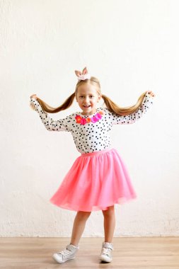 Paskalya bunny kulaklar kafa, renkli puantiyeli gömlek ve pembe tutu etek giymiş uzun sarı saçlı sevimli küçük beş yaşındaki kız portresi. Beyaz duvar backgroung, kopya alanı, yakın çekim.