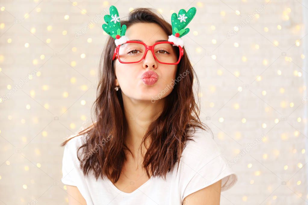 Beautiful young woman wearing santa claus furry hat & masquerade glasses for Chritmas celebration event. Attractive female being silly, making faces at dress up party. Background, close up, copy space