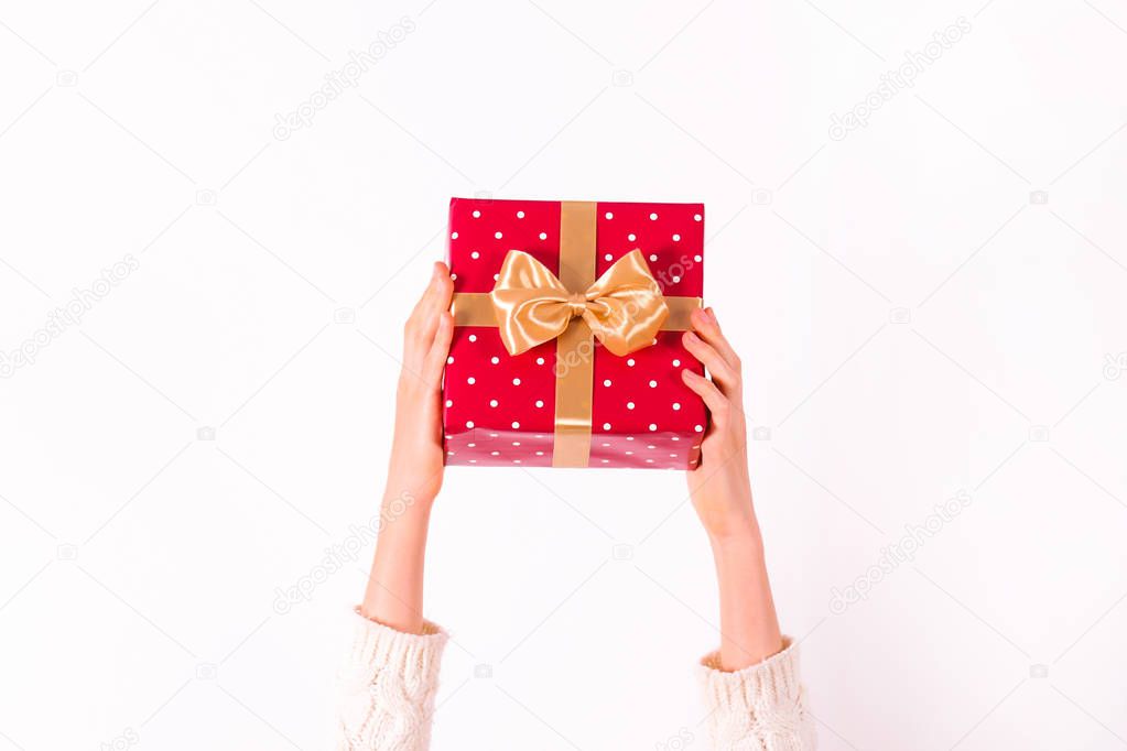 Female hands holding present with golden bow on white rustic background. Festive template for different holidays: Christmas, New Year, Birthday, Valentines day,. Close up, copy space, top view.