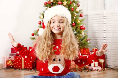 Portre sevimli mutlu dokuz yaşındaki kızın birçok kırmızı Noel kazağı giymiş sunar, zemin üzerine sarılmış hediyeler yığını ile süslenmiş Noel ağacı. Yakın çekim, alanı Kopyala.