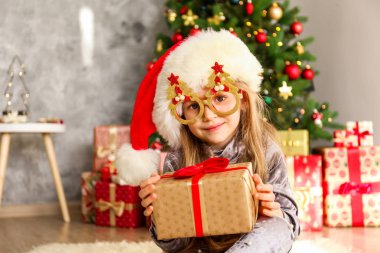 Portre sevimli mutlu beş yaşındaki kızın birçok alan sunar, zemin üzerine sarılmış hediyeler yığını ile süslenmiş Noel ağacı. Yakın çekim, alanı Kopyala.