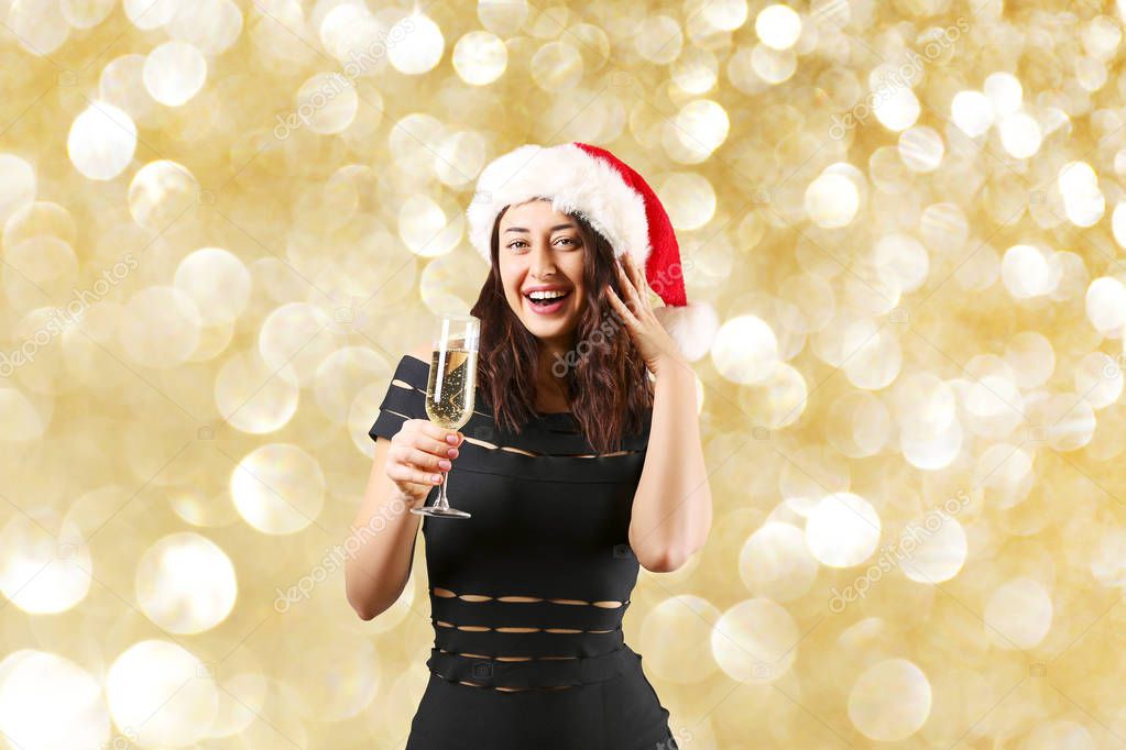 Portrait of young attractive woman wearing black tight sexy dress Santa Claus hat Drinking champagne and celebrating Christmas. Festive background, copy space, close up. Christmas mood concept.
