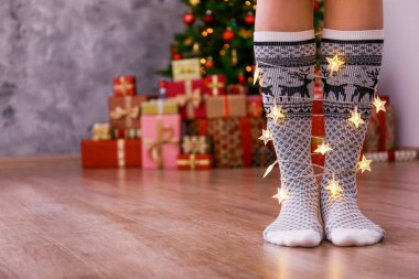 Ren geyiği yazdırma ve süsleme, dekore Noel ağacına arka plan ile Orta buzağı çorap giyen sarılı, ışıklar ile ayakta kadın bacak atış kırpılmış. Uzay kopyalayın, yakın çekim.