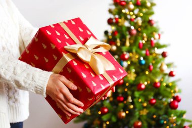 Atış tanınmaz halde genç kadının beyaz örgü kazak giyen kırpılmış, Festival kırmızı kaydırmalı hediye tutarak Altın Yay, arka plan üzerinde Noel ağacı ile bağlı. Yakın çekim, alanı Kopyala.