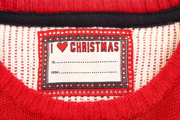 Ugly christmas sweater as a present concept. Cropped shot of neck hole with blank from to fields name tag. Festive red knitted jumper. Top view, close up, copy space.