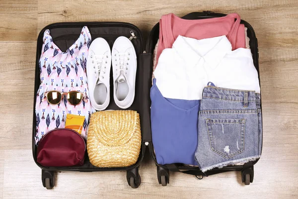 Open suitcase fully packed with folded women\'s clothing and accessories on the floor. Woman packing for tropical vacation concept. Female luggage w/ things. Background, close up, copy space, top view.