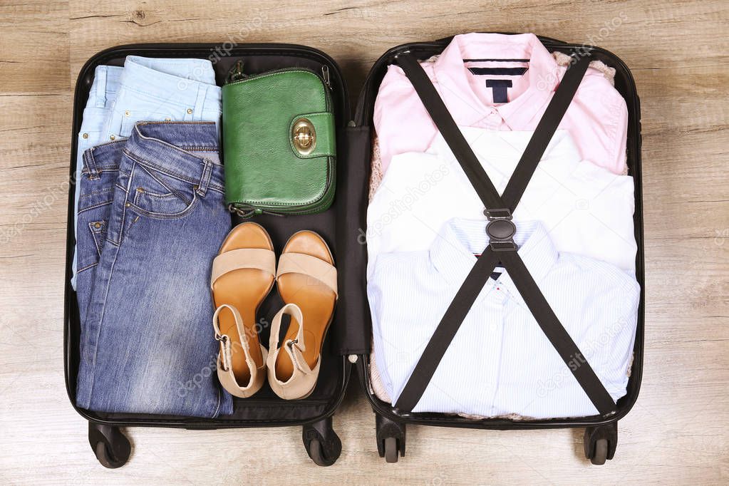 Open suitcase fully packed with folded women's clothing and accessories on the floor. Woman packing for business trip concept. Female luggage w/ things. Background, close up, copy space, top view.