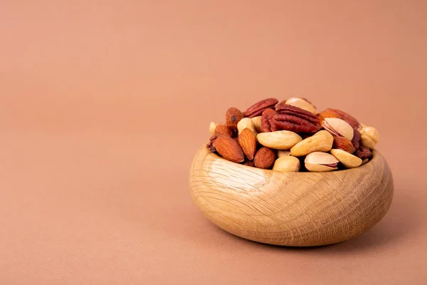 Mixed nuts in wooden bowl and scattered on table. Trail mix of pecan, almond, macadamia & brazil edible nuts with walnut hazelnut on wood textured surface. Background, copy space, top view, close up.