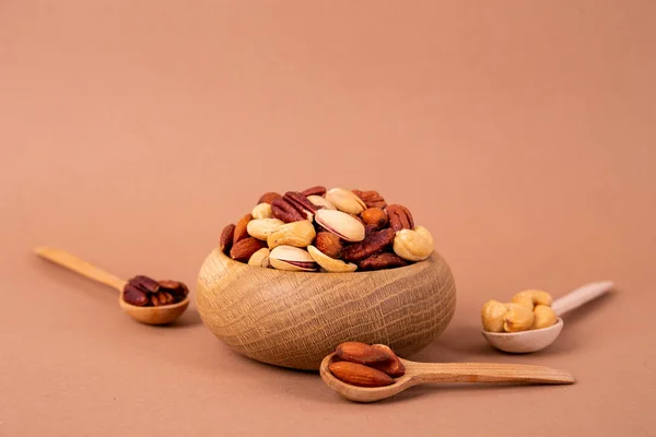 Mixed nuts in wooden bowl and scattered on table. Trail mix of pecan, almond, macadamia & brazil edible nuts with walnut hazelnut on wood textured surface. Background, copy space, top view, close up.
