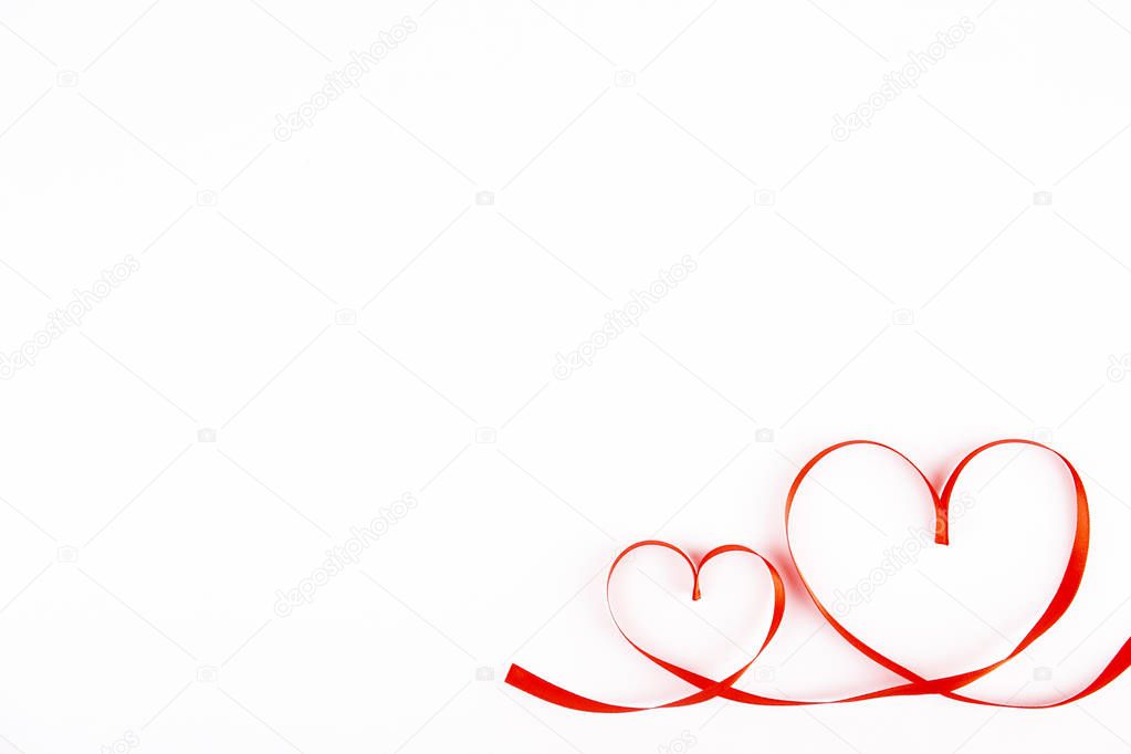Isolated silk red ribbon laid in heart shape on bright white background. Festive decoration. Mother's, Women's, Wedding, Happy st Valentines Day concept, 14th February. Top view, flat lay, close up.