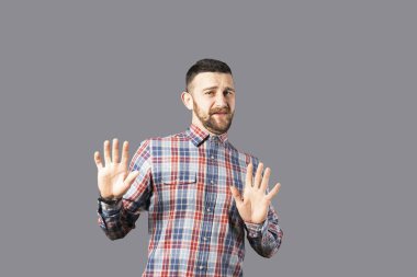 Beden dili kavramı. Yakışıklı delikanlı sakal duygular gösterilen gri duvardan poz ile. Erkeksi sakallı erkek portresi, ince giyen kareli gömlek uygun. İzole arka plan, kopya alanı