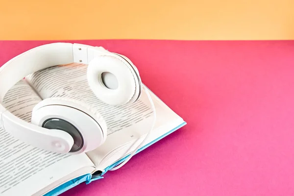 Electronic audiobook vs regular paper book concept. Stack of different color hardcover books with blank colorful covers & white headphones on table. Old versus new. Close up, copy space, background.