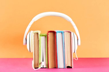 Elektronik audiobook vs normal kağıt kavramı kitap. Tablo boş renkli kapakları ve beyaz kulaklık ile farklı renk ciltli kitap yığını. Eski ve yeni. Yakın çekim, uzay, arka plan kopya.