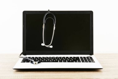 Modern tıbbi yazılım ve teknoloji gelişmeler kavram. Doktor çalışma tablo, stetoskop, boş ekran dizüstü bilgisayar. Akustik tıbbi cihaz, ahşap masaüstü bilgisayarda. Yakın çekim, uzay, arka plan kopya.