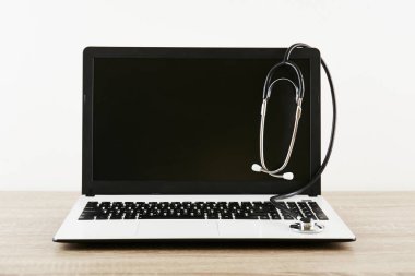 Modern tıbbi yazılım ve teknoloji gelişmeler kavram. Doktor çalışma tablo, stetoskop, boş ekran dizüstü bilgisayar. Akustik tıbbi cihaz, ahşap masaüstü bilgisayarda. Yakın çekim, uzay, arka plan kopya.