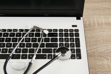 Modern tıbbi teknoloji ve yazılım gelişmeler kavram. Doktor çalışma tablosu stetoskop akustik cihazla, laptop klavye yakın ahşap masaüstünde. Kopyalama alanı, arka plan, üstten görünüm, düz yatıyordu.