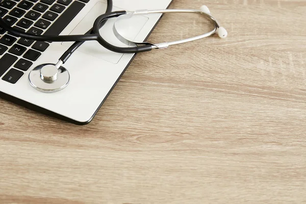 Modern medical technology and sofware advances concept. Doctor's working table with stethoscope acoustic device, laptop keyboard close up on wooden desktop. Copy space, background, top view, flat lay.