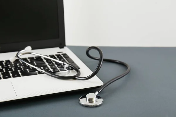 Modern medical sofware and technology advances concept. Doctor's working table, stethoscope, blank screen laptop. Acoustic medical device, computer on wooden desktop. Close up, copy space, background.