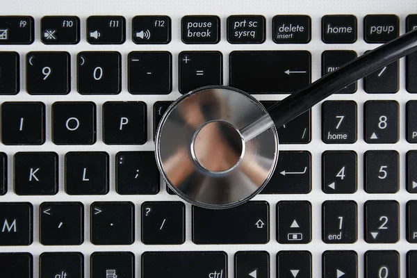 Modern medical technology and sofware advances concept. Computer and gadget diagnostics and repair. Close up of stethoscope acoustic device testing laptop keyboard. Top view, copy space, background.