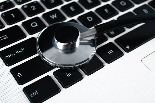 Modern medical technology and sofware advances concept. Computer and gadget diagnostics and repair. Close up of stethoscope acoustic device testing laptop keyboard. Top view, copy space, background.