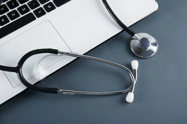 Modern medical technology and sofware advances concept. Doctor\'s working table with stethoscope acoustic device, laptop computer keyboard close up. Copy space, background, top view, flat lay.