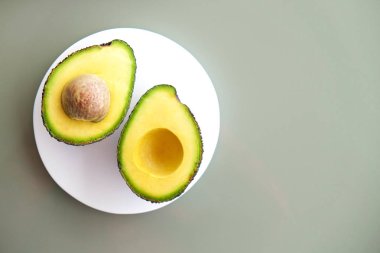 Beyaz mermer coaster ile yarıya besin yoğun avokado meyve dilimleri kalp sağlıklı tekli doymamış yağ gri cam masa üstü dolu. Yakın çekim, kopya alanı, üstten görünüm, arka plan.