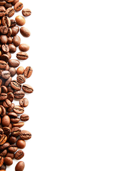 Roasted brown coffee beans scattered on white table with a lot copy space for text. Flat lay composition. Close up, top view, background.