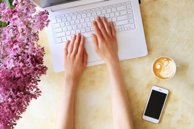 Beyaz dizüstü bilgisayar, beton dokulu masa arka plan üzerinde yazarak kadın üst görünüm. Çiçek buketi ile kadınsı çalışma alanı. Kapat, kopyalama alanı.