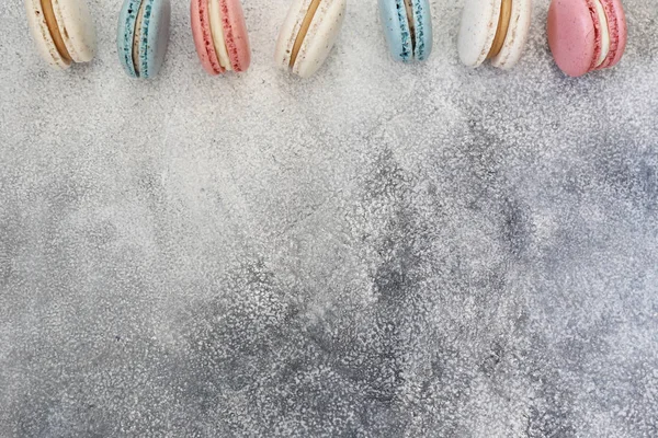 Composición minimalista con manojo de dulces macaron franceses de diferente color y sabor formando un marco sobre fondo de textura de hormigón grueso. Vista superior, primer plano, plano, espacio para copiar . —  Fotos de Stock