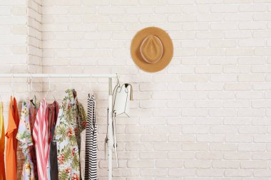 Kadın kalçalı giyim mağazasının iç mekanı. Alışveriş merkezindeki hippi moda şovu odasında askıda asılı renkli kadın kıyafetleri. Beyaz tuğlalı arka plan. Boşluğu kopyala.
